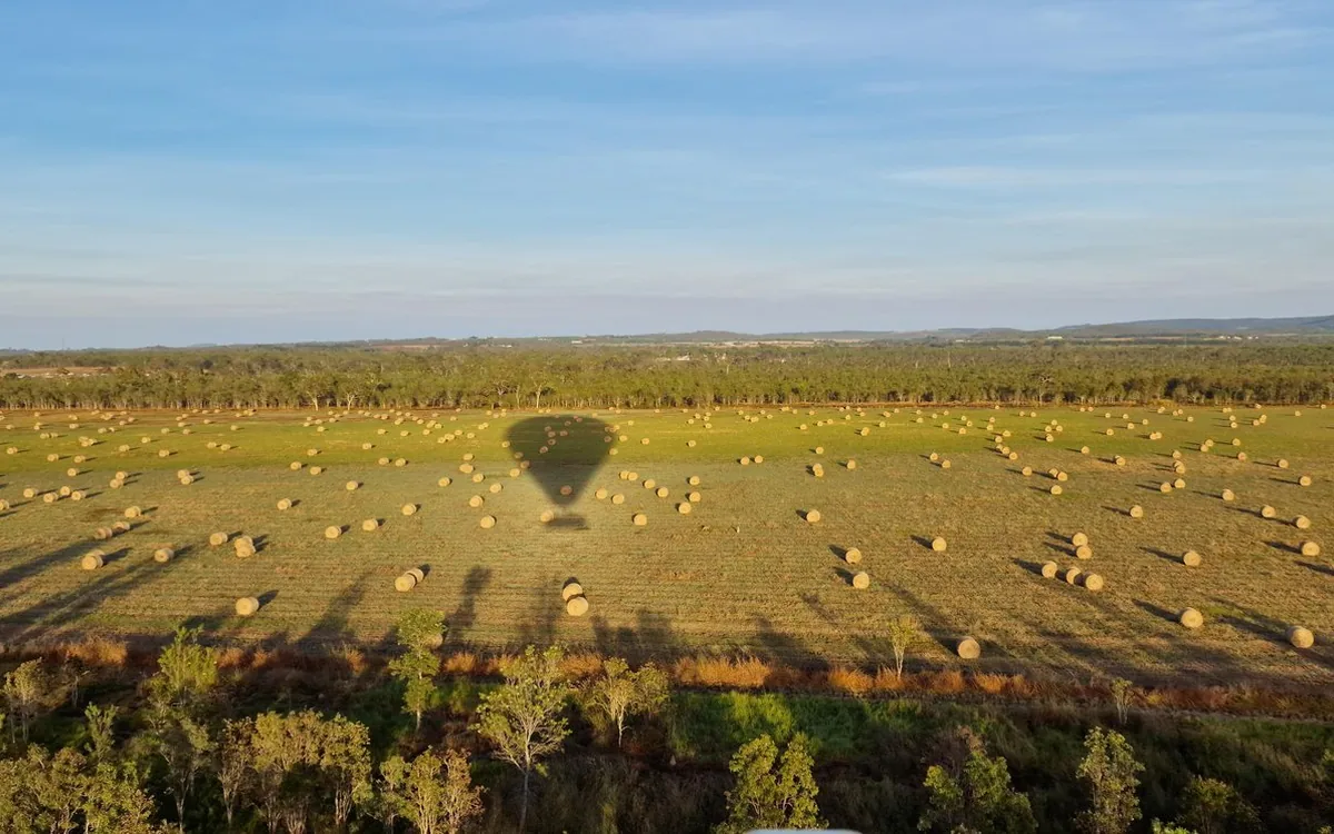 The shadow of a hot air balloon crossing harvested fields dotted with hay bales