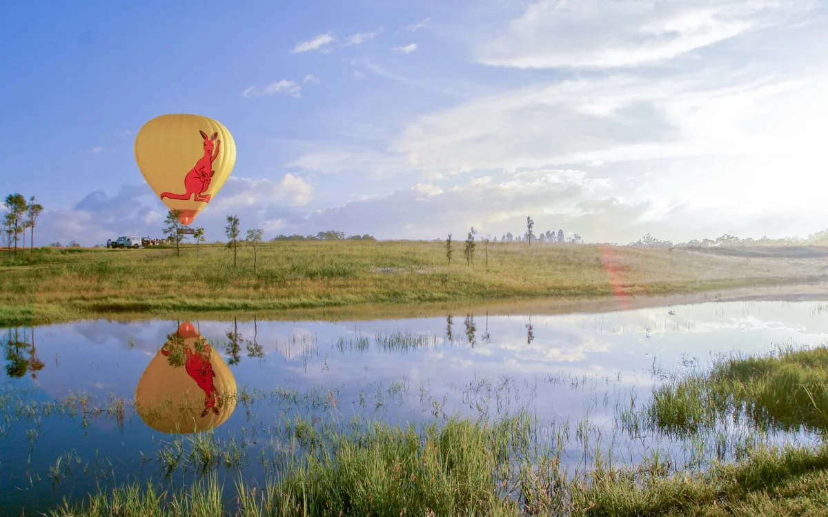 A hot air balloon low over still water on the tablelands, mirrored in the surface
