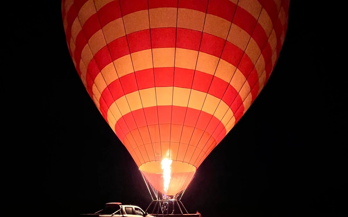 A striped hot air balloon envelope lit from inside by the burner against a dark sky