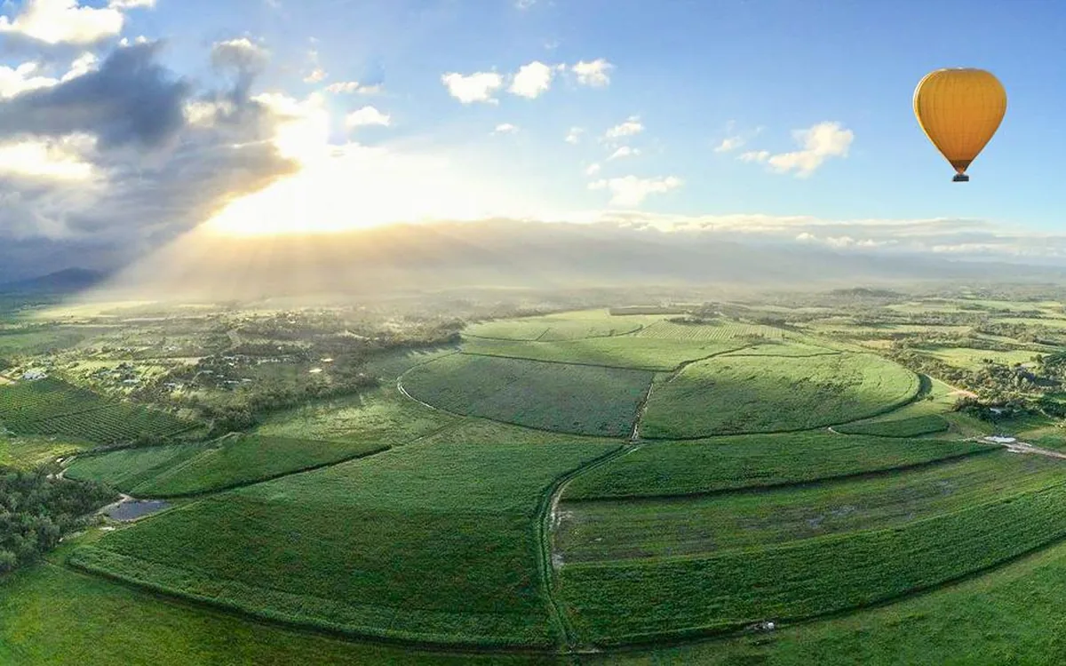 Green farmland on the Atherton Tablelands from the air, with one hot air balloon at cloud level