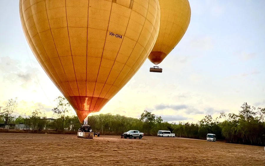 A hot air balloon standing on a bare field at first light, cars parked behind it