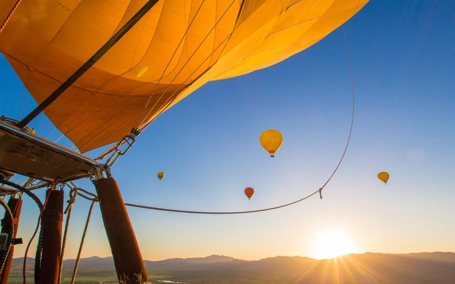 Balloons in the air at dawn, seen past the yellow fabric of another envelope