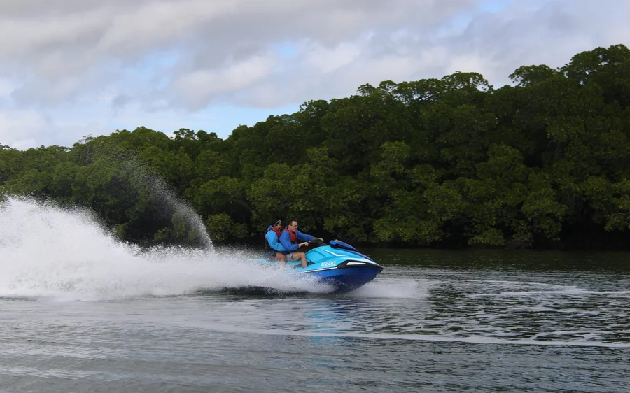 A jet ski throwing up spray on a river between mangroves