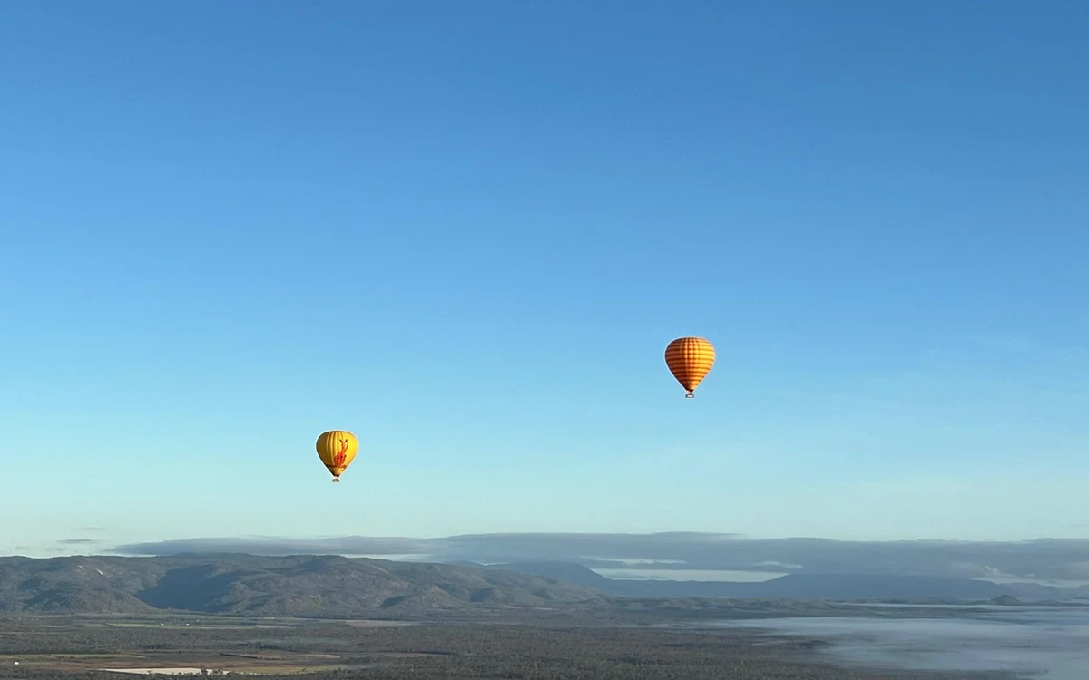 Two hot air balloons high above a wide hazy valley with hills on the horizon